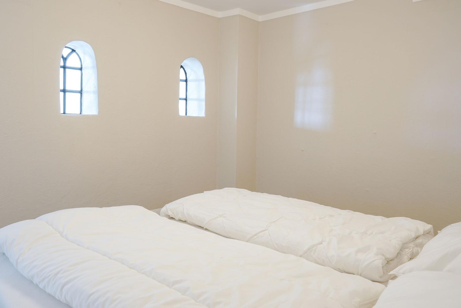 Zimmer mit weißem Bett und zwei Bogenfenstern an der Wand.
