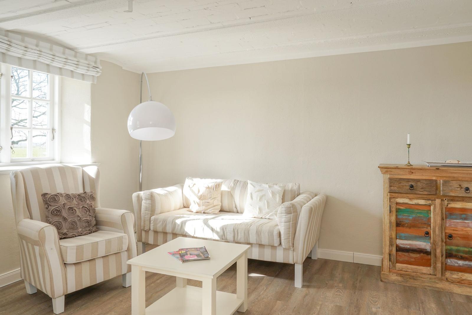 Wohnzimmer mit Sofa, Sessel, Tisch und Schrank. Fenster mit Rollladen. Holzboden und weiße Wände.
