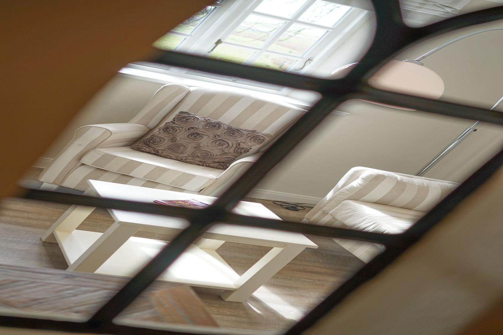 Ein Wohnzimmer mit Sofa, Couchtisch und Fenster. Blick durch ein Gitter.