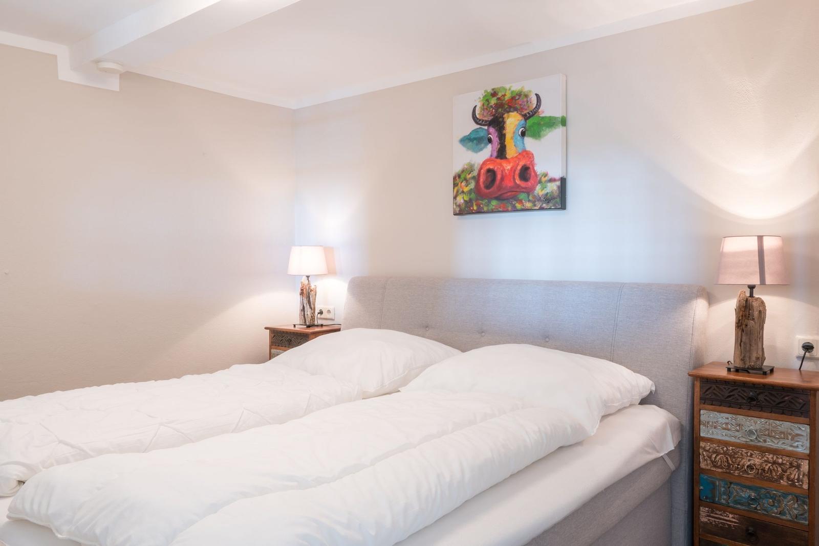 Schlafzimmer mit Bett, Nachttischen und Wandbild einer Kuh.