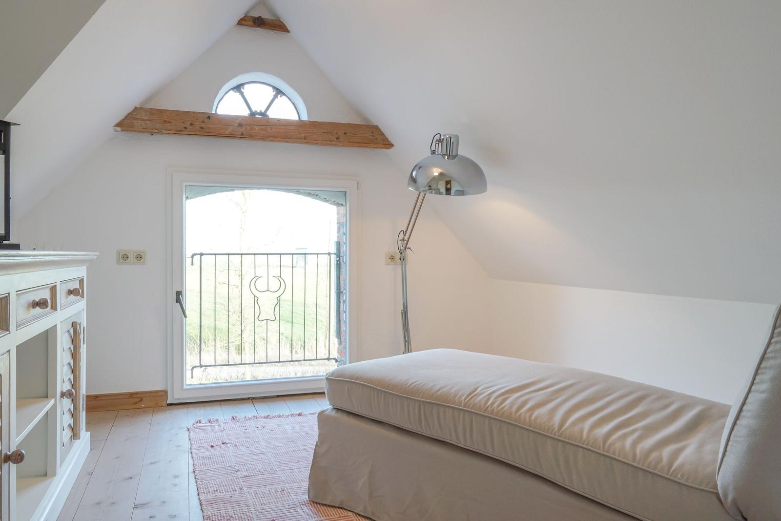 Schlafzimmer mit Dachschrägen, Fenster und Bett. Holzboden und Stehlampe.