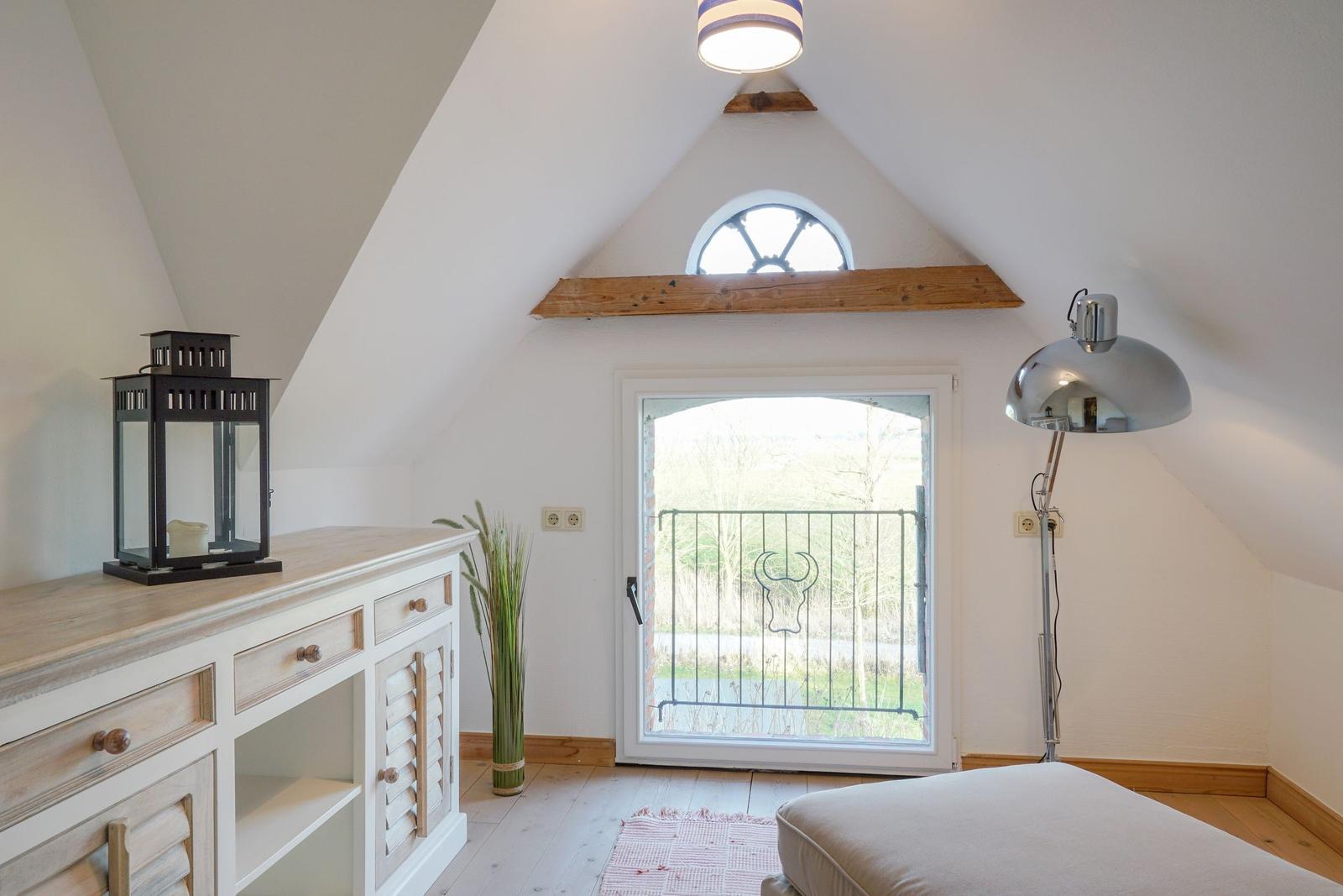 Zimmer mit Dachschräge, Fenster zur Terrasse und Schreibtisch mit Laterne.