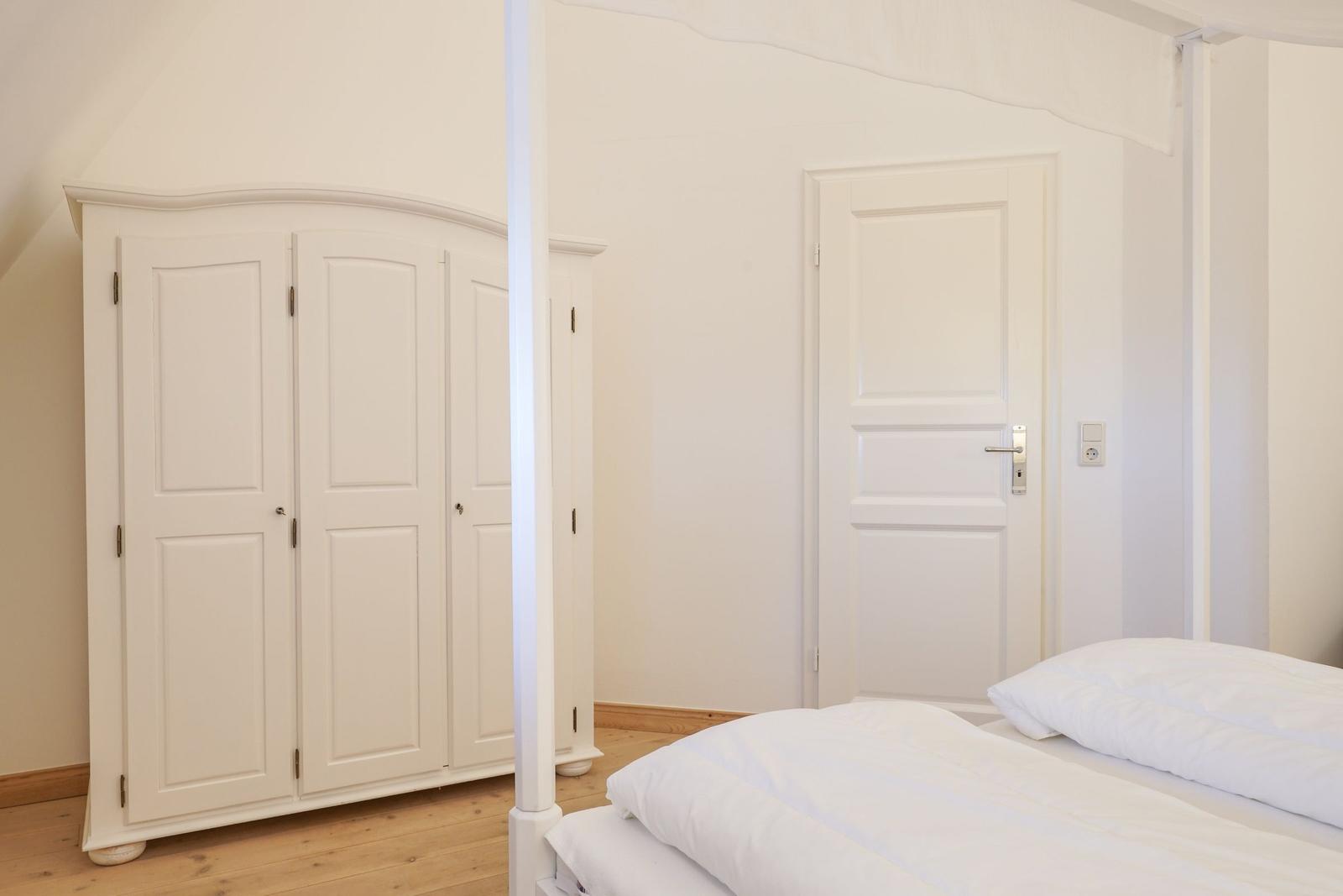Schlafzimmer mit weißem Bett, Kleiderschrank und Tür