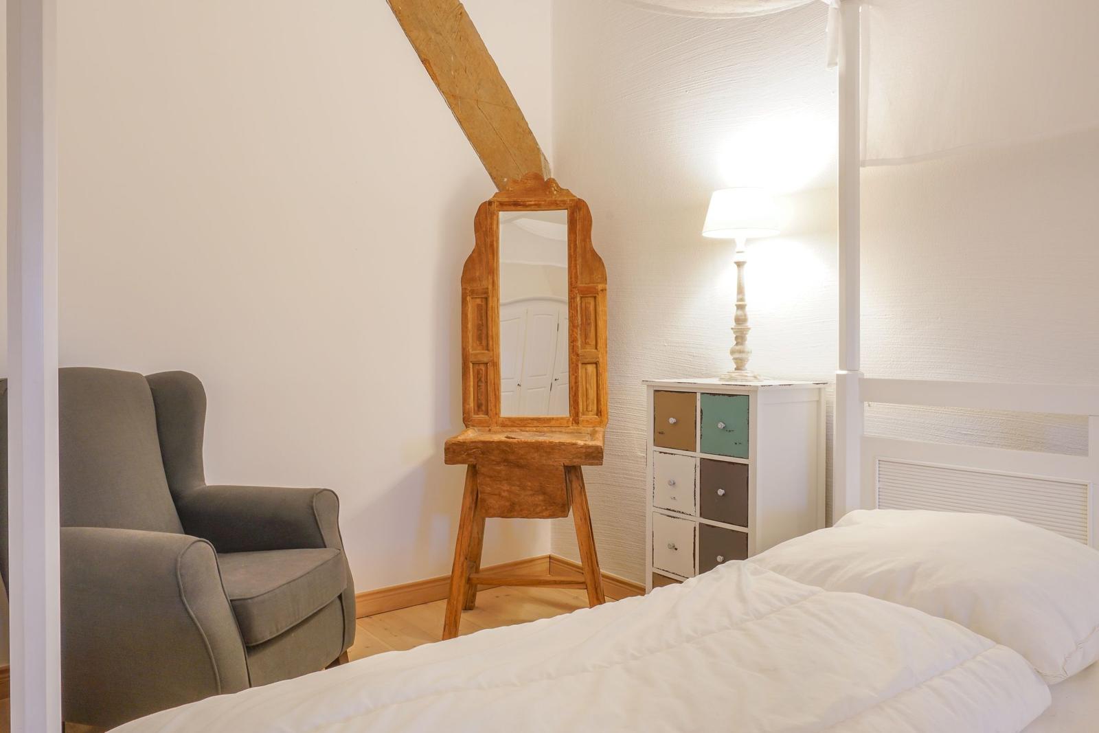 Schlafzimmer mit Bett, Sessel, Spiegel und Nachttisch.