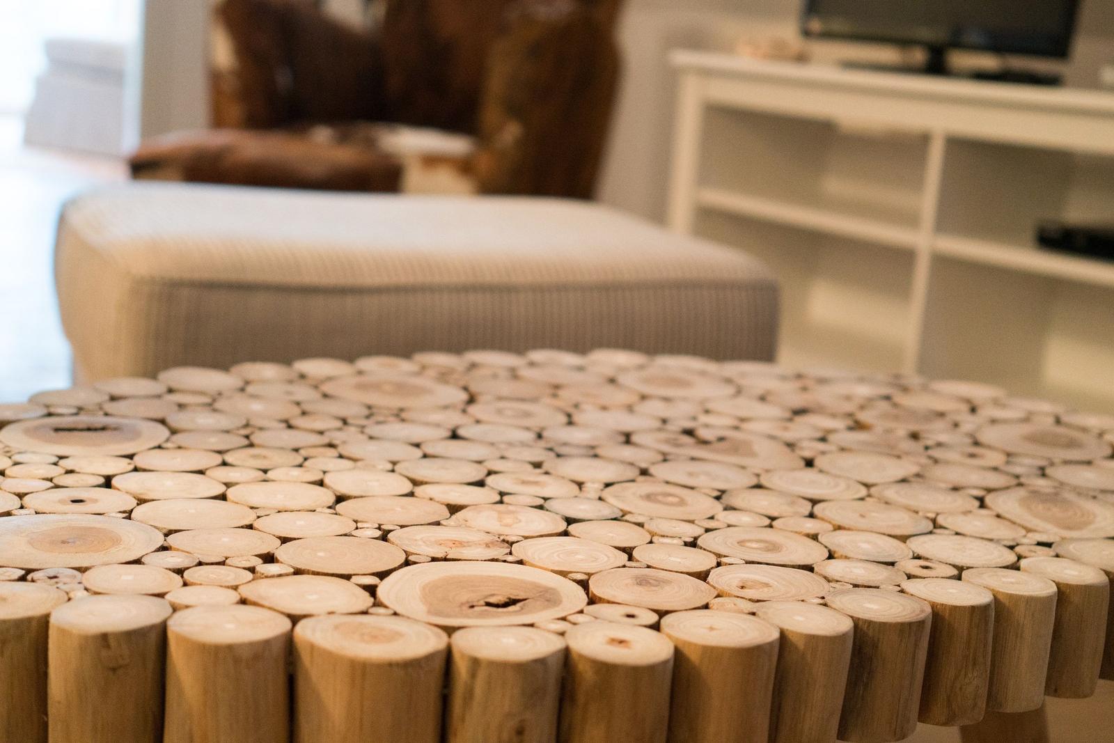 Holztisch aus Baumstämmen im Wohnzimmer mit Sitzbank und Fernsehregal im Hintergrund.