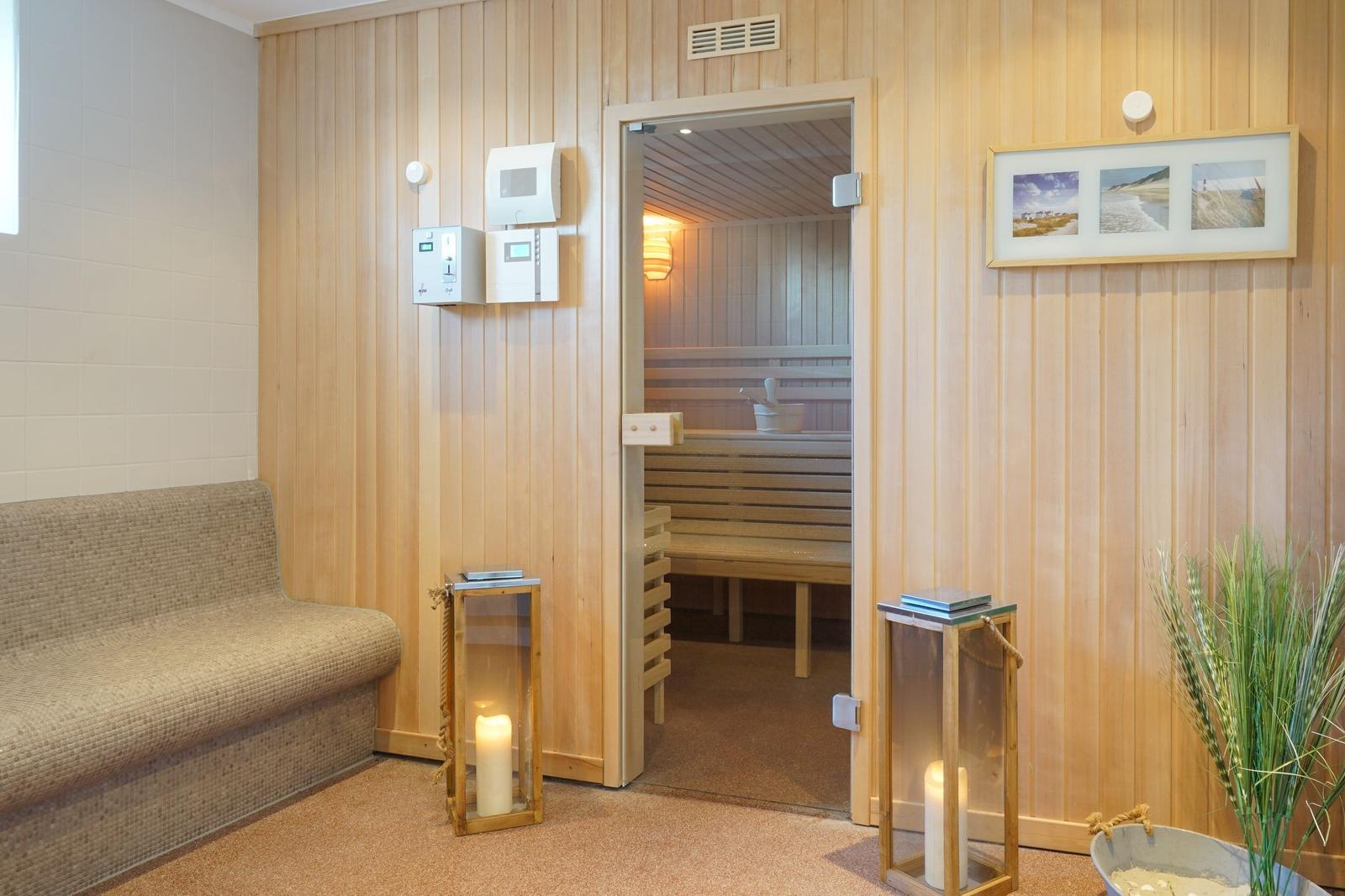 Sauna mit Holzwand und Sitzbänken. Vorraum mit Sofa, Kerzen und Pflanze.