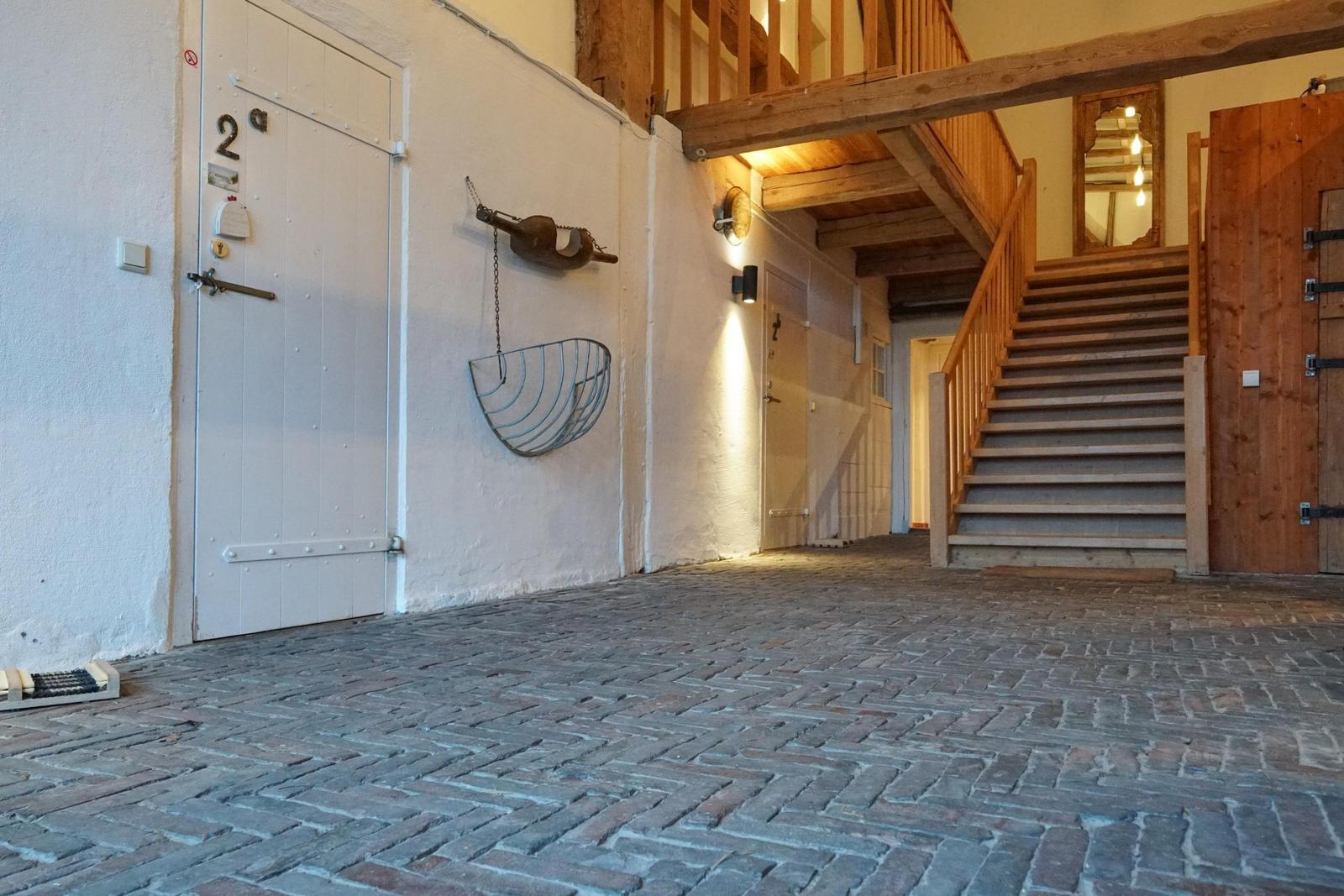 Helle Eingangshalle mit Steinboden, Holztreppe und rustikalen Wanddekorationen.