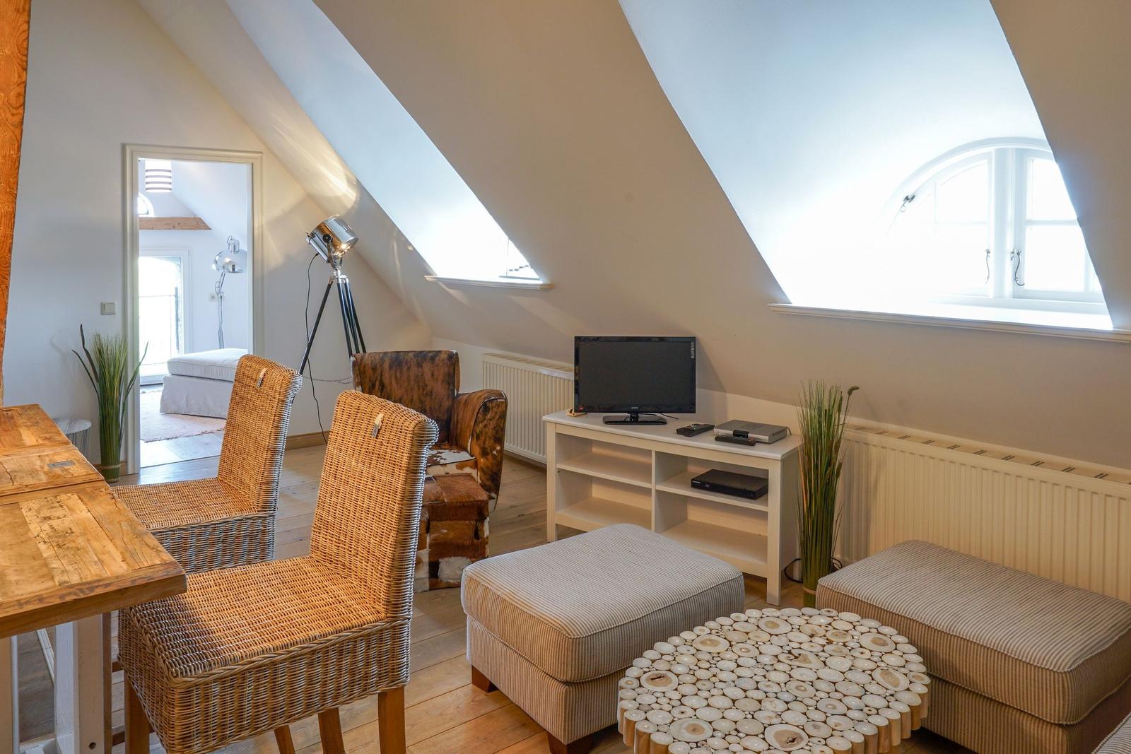 Dachgeschosszimmer mit TV, Sitzgelegenheiten und Dachfenstern.