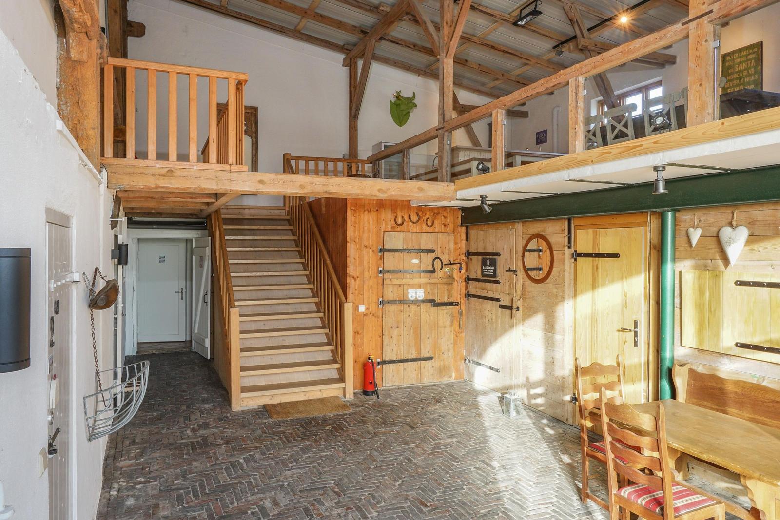 Erdgeschoss mit Holztreppe, Tisch und Stühlen sowie Obergeschoss mit Balkon.