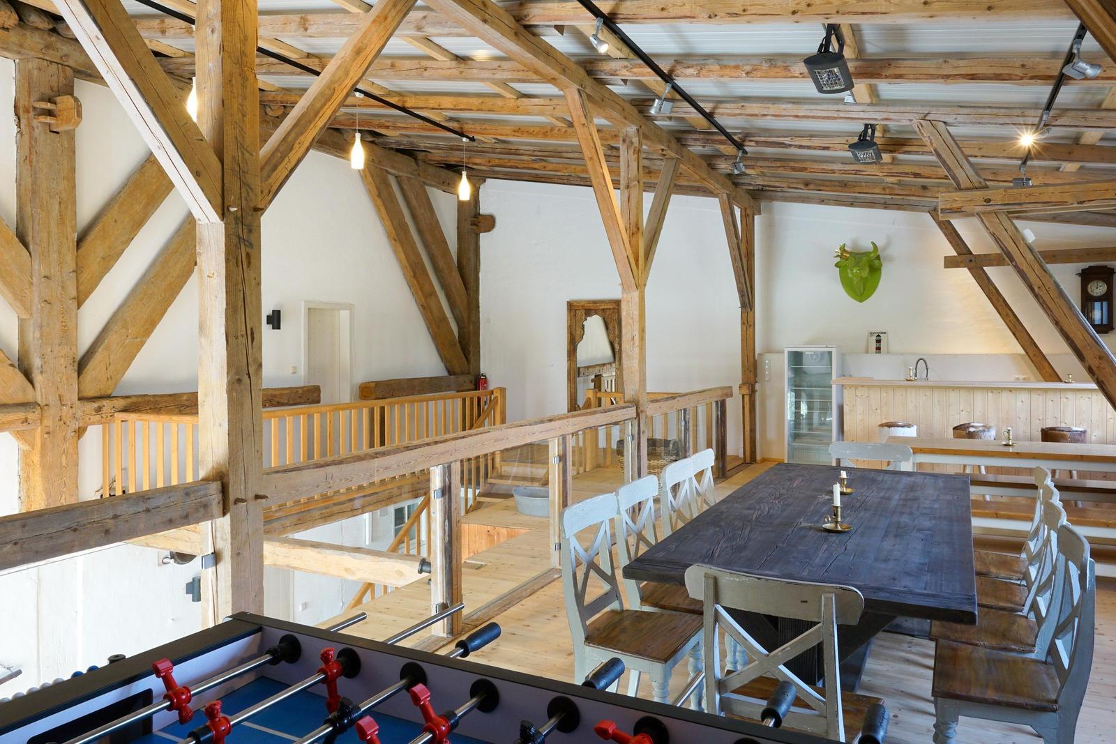 Großer Raum mit Holzrahmen, Esstisch und Küchenbereich. Spielzimmer mit Tischfußball.