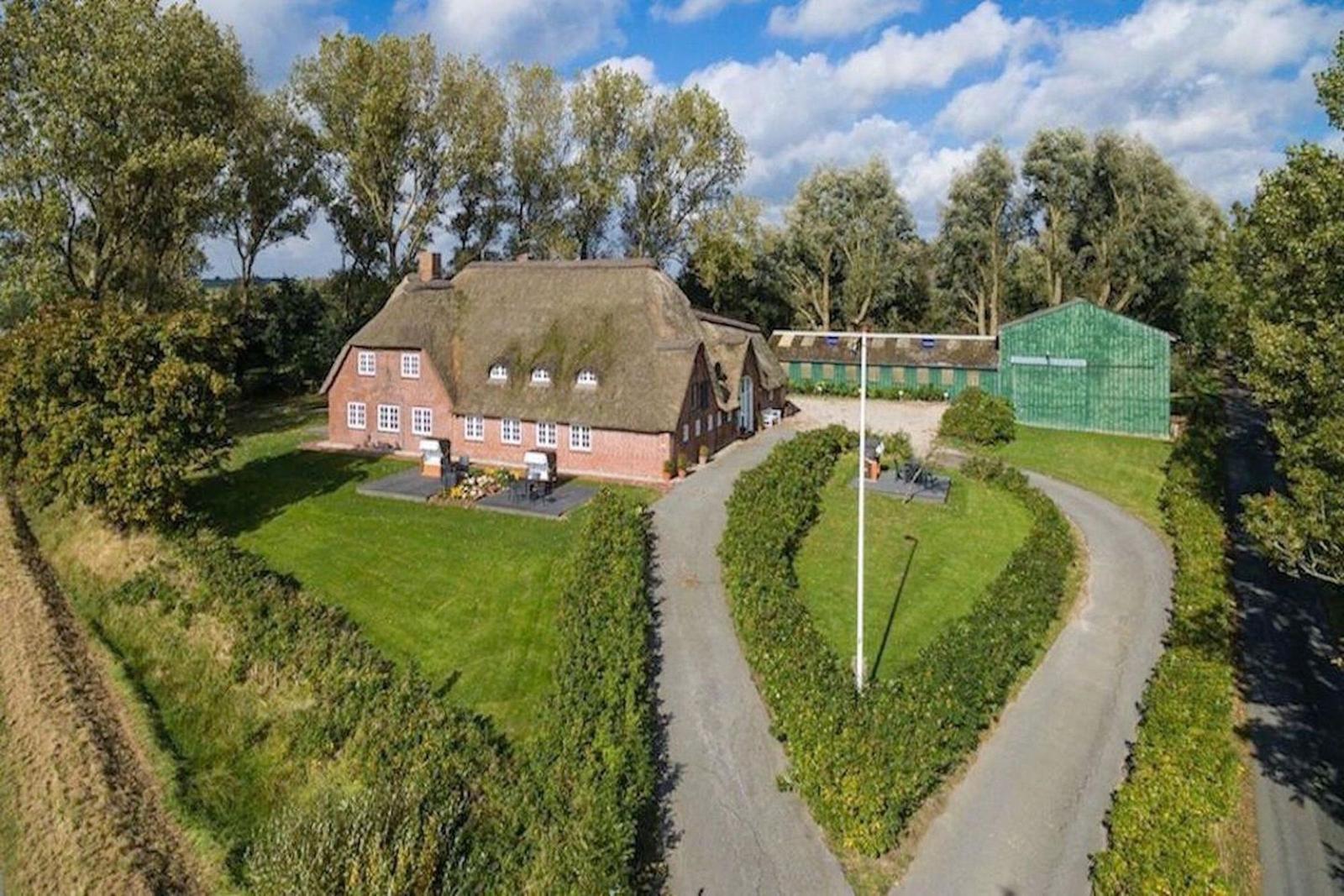 Haus mit Strohdach, grüner Garten und Weg. Nebenan steht ein grüner Schuppen.