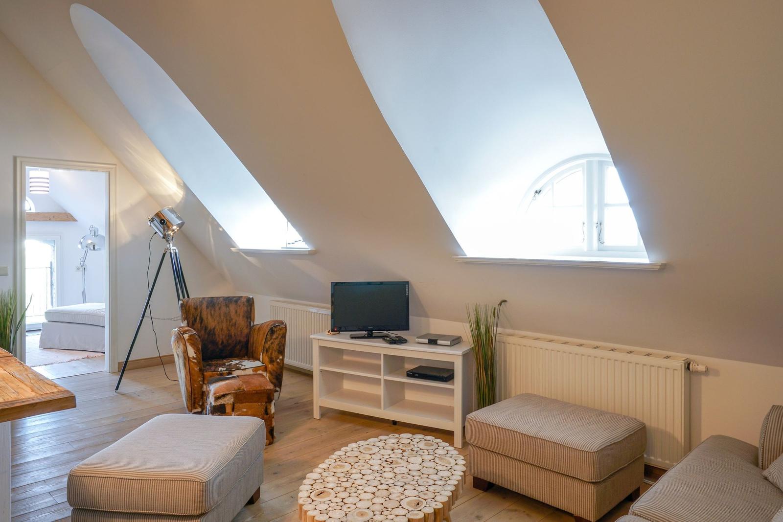 Wohnzimmer mit schrägen Dachfenstern, Sofa, Sessel und Fernseher.