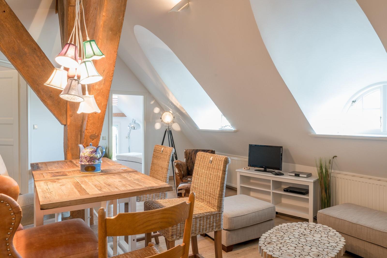 Dachgeschosswohnung mit Essbereich, TV und Sitzgelegenheiten unter schrägen Dachfenstern.
