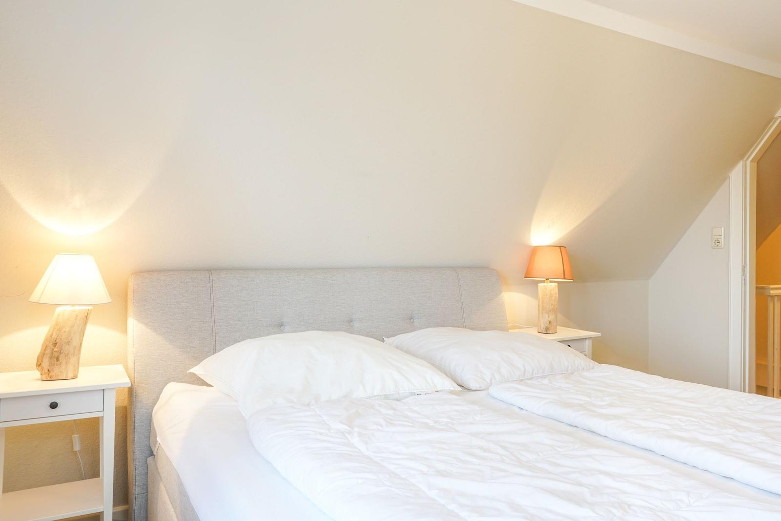 Schlafzimmer mit Bett, zwei Nachttischen und Lampen an den Seiten.