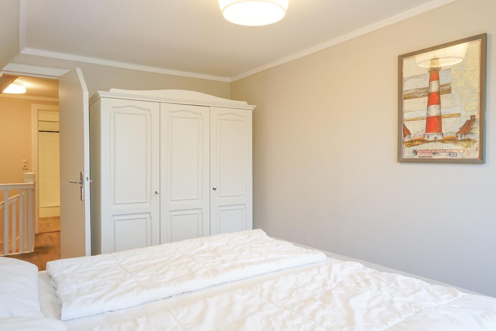 Schlafzimmer mit weißem Bett, Kleiderschrank und Leuchtturm-Bild an der Wand.