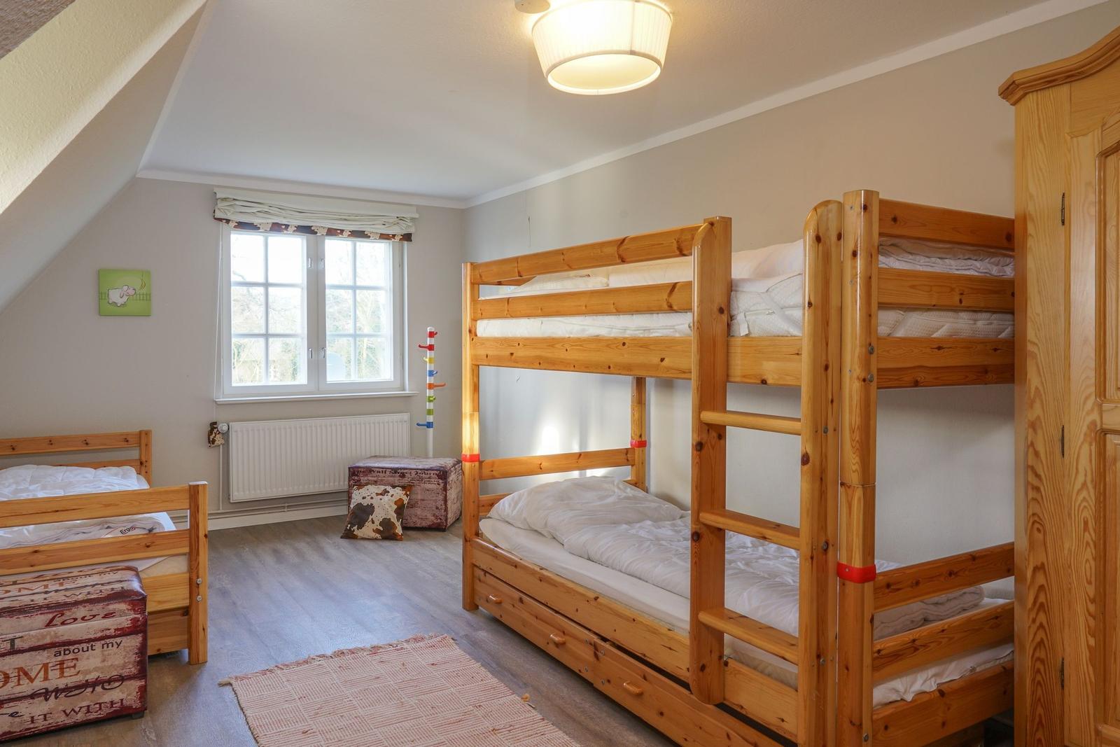 Zimmer mit Doppelstockbett und Einzelbett, Fenster, Kleiderschrank und Bodenbelag.