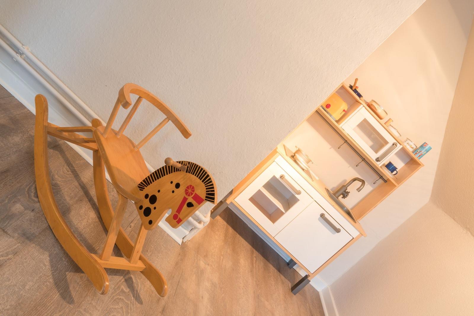 Ein hölzerner Schaukelpferd und ein Kinderspielküchenmöbel stehen im Raum.