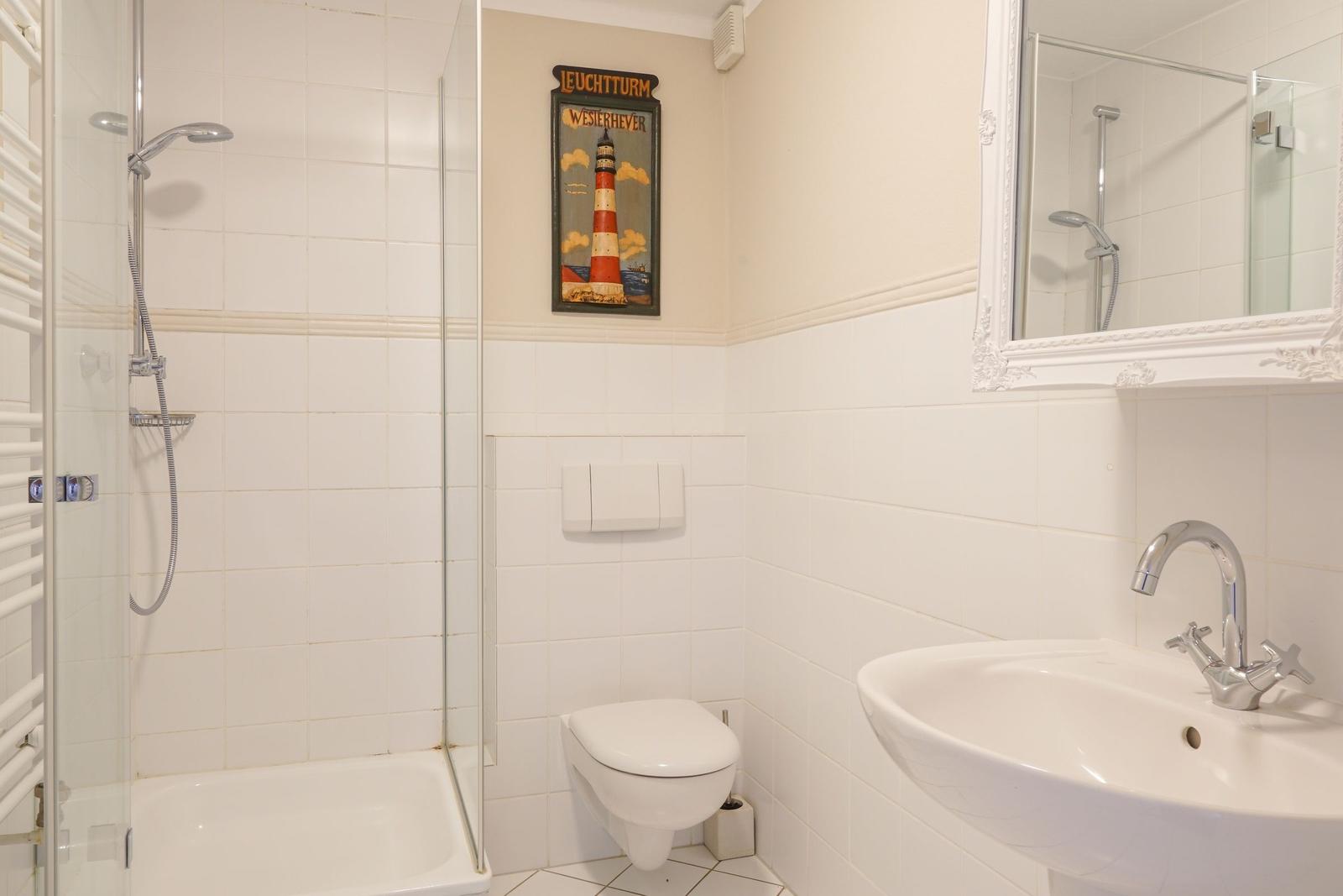 Badezimmer mit Dusche, Toilette und Waschbecken. Wandbild zeigt Leuchtturm Weserhever.