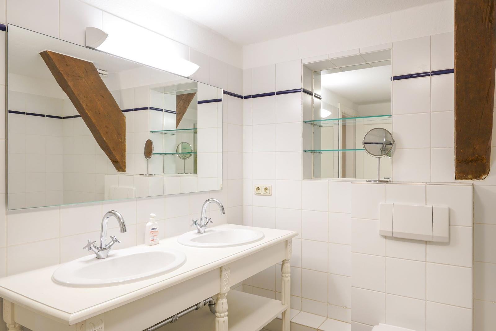 Badezimmer mit zwei Waschbecken, Spiegeln und Holzbalken an den Wänden.
