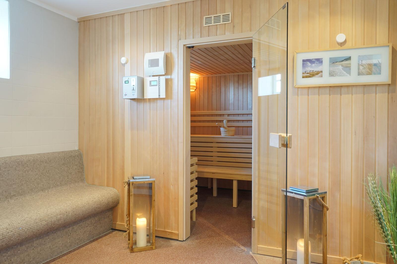 Sauna mit Holzwand, Sitzbänken und Glaswand. Nebenraum mit Sofa und Kerzen.