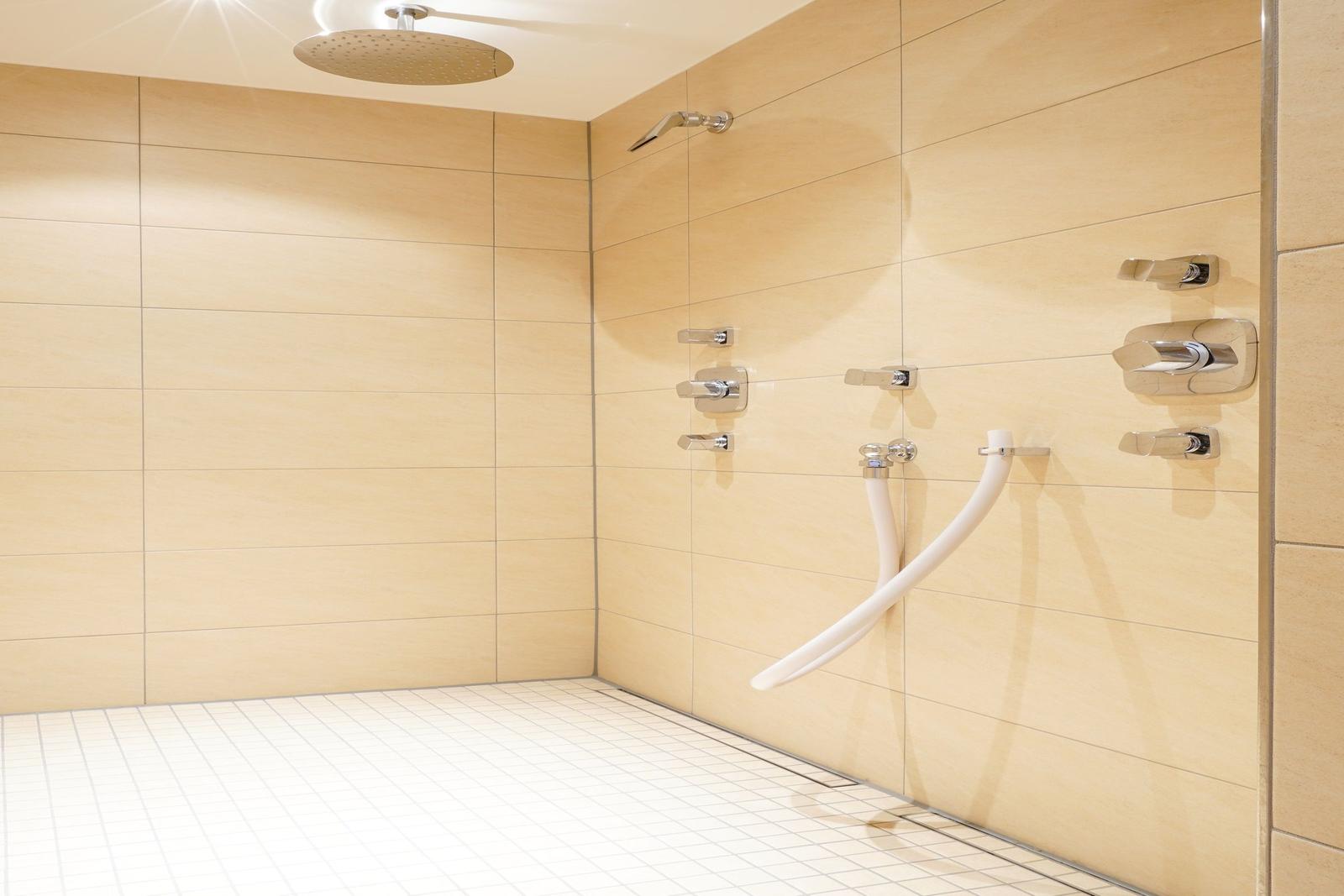 Dusche mit Dachduschkopf, Wandhalterungen und Bodenfliesen.