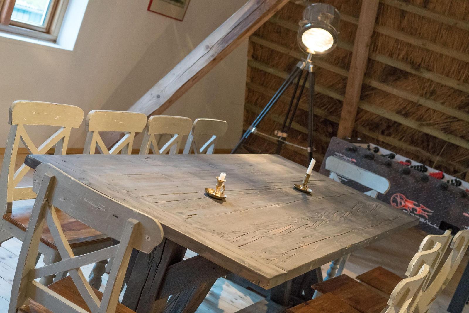 Holztisch mit Stühlen, Stehlampe und Tischkästchen in Raum mit Dachschrägen und Fachwerk.