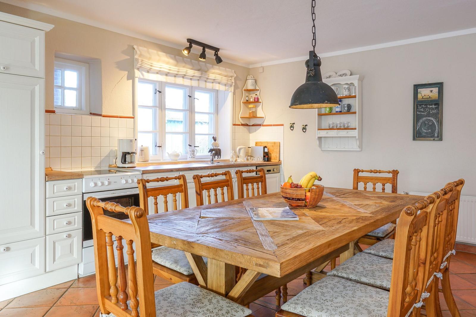 Küche mit Essbereich, Holztisch, Stühle, Fenster und Küchengeräte.