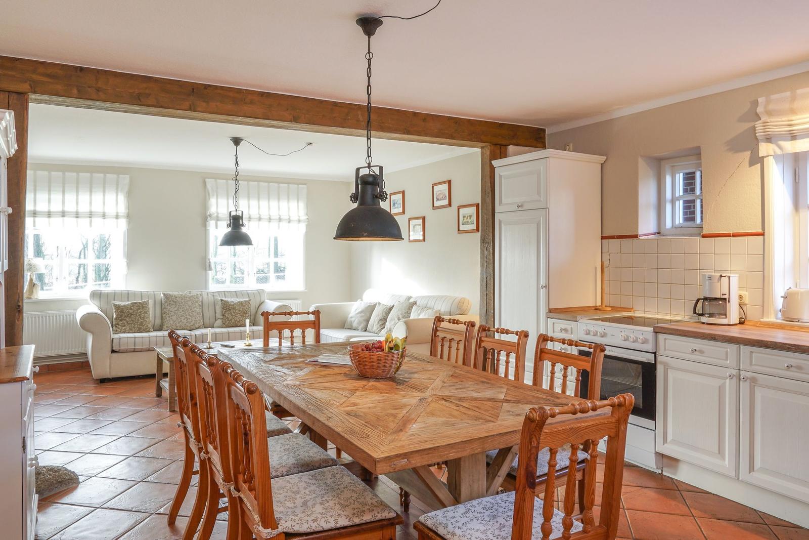 Essbereich mit Holztisch und Stühlen. Küche mit weißen Schränken. Wohnzimmer im Hintergrund.