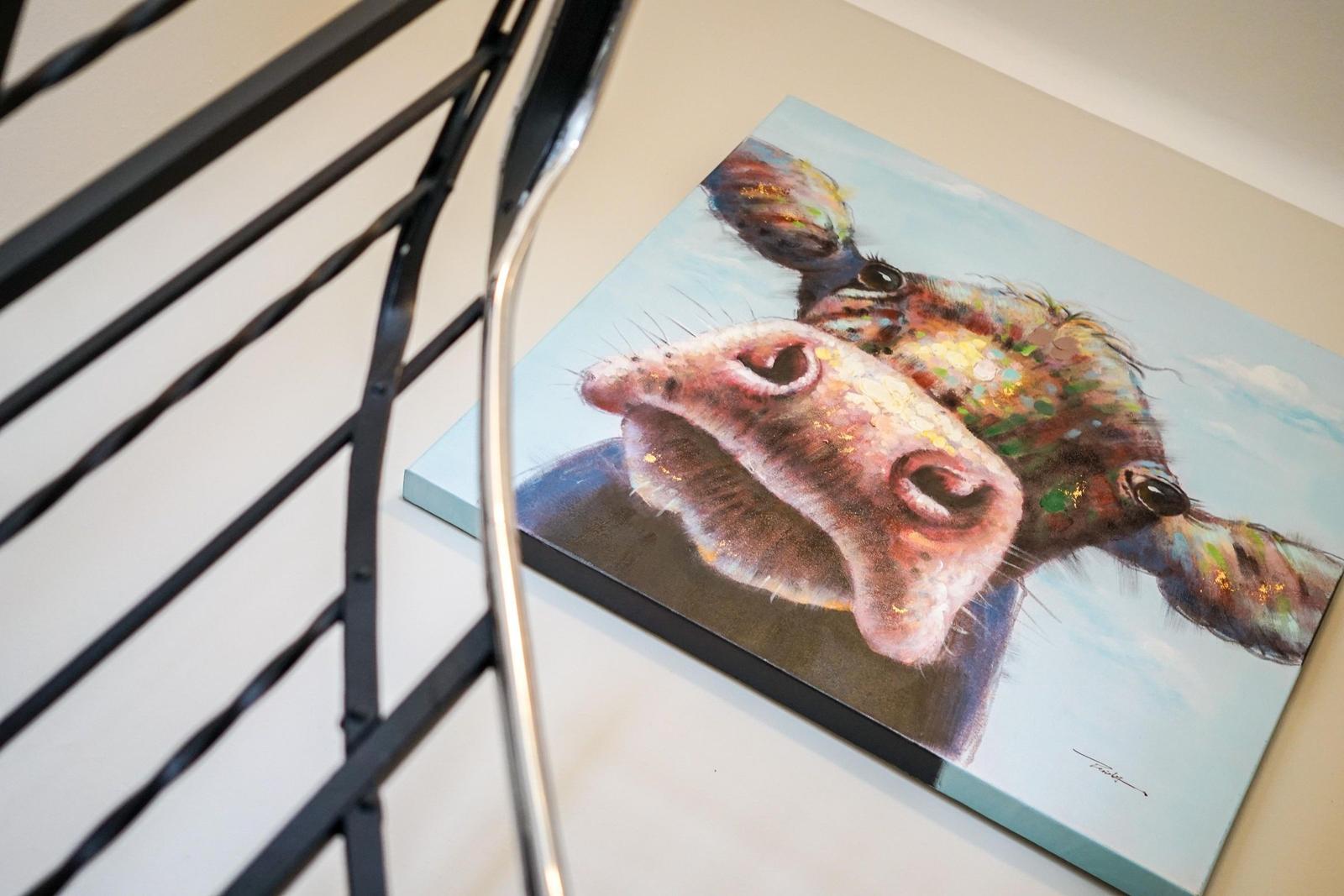 Ein Wandbild mit einem Kuhkopf, das an einer Wand neben einem Metallgeländer hängt.
