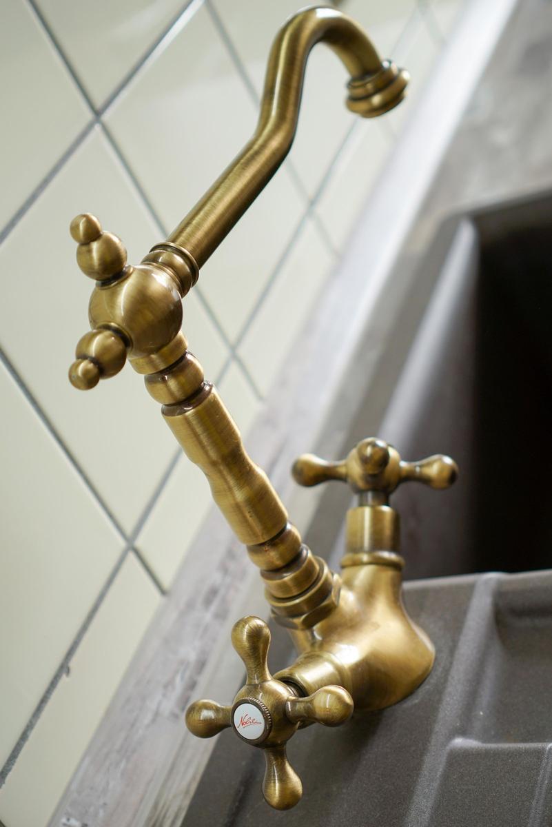 Antik-goldener Wasserhahn mit zwei Griffen über einem Küchenspülbecken.