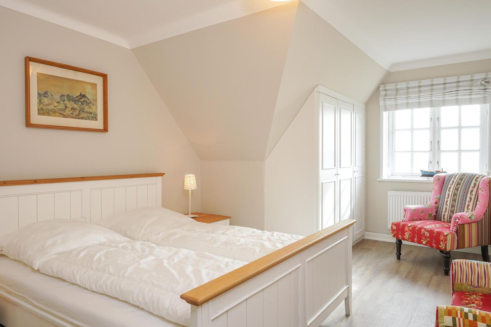 Schlafzimmer mit Doppelbett, Schrank und Sessel vor Fenster.