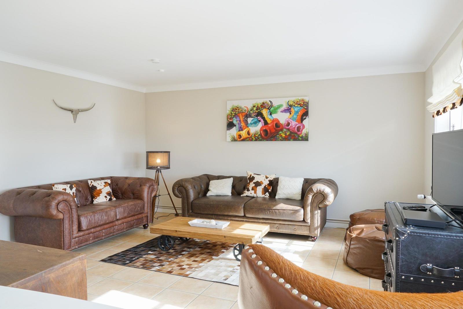Wohnzimmer mit zwei Ledersofas, Holztisch und Wandbild mit Rindern.