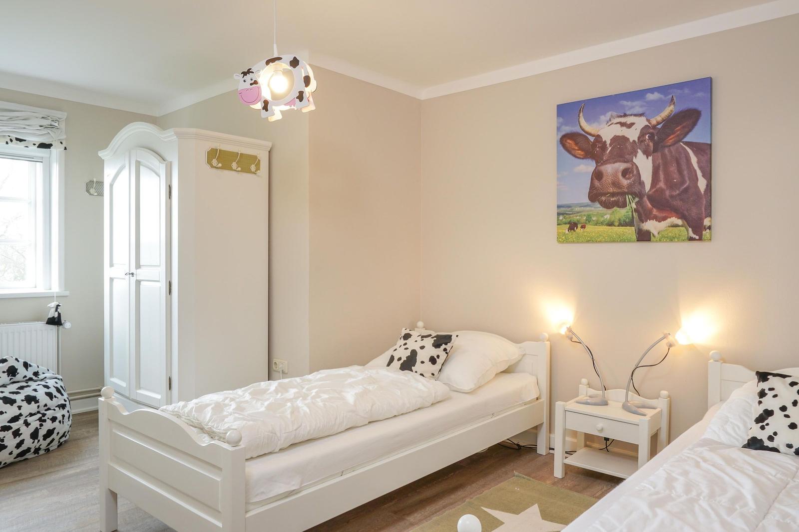Zwei Einzelbetten mit Kuhmotiven, Wandbild und Schrank im Schlafzimmer.