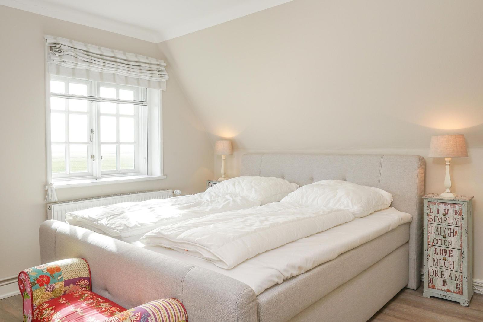 Schlafzimmer mit Bett, Fenster und Nachttisch mit Lampe.
