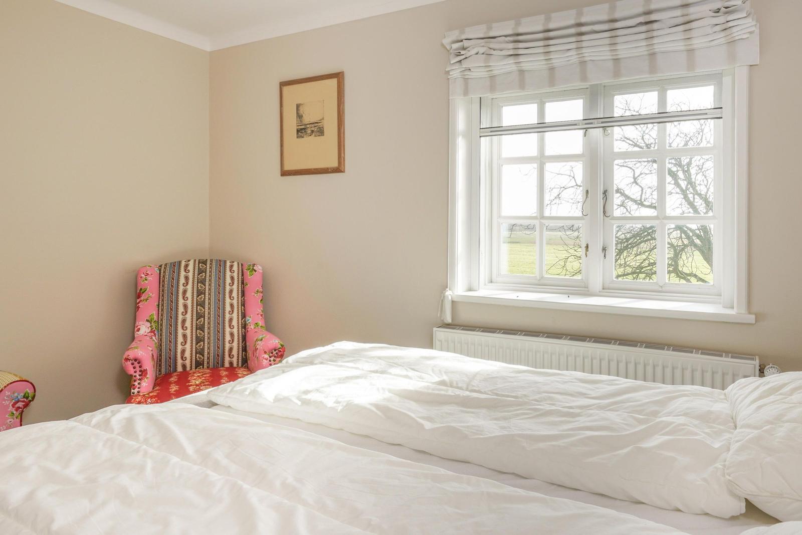 Schlafzimmer mit Bett, Fenster und Stuhl mit buntem Stoff.