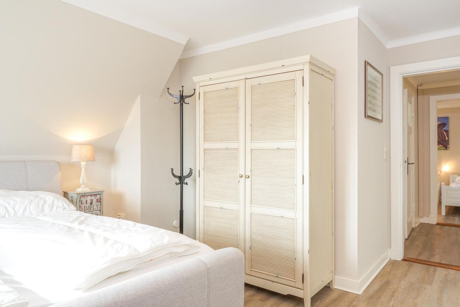 Schlafzimmer mit Bett, Kleiderschrank und Stehlampe. Durchgang zu weiteren Räumen.