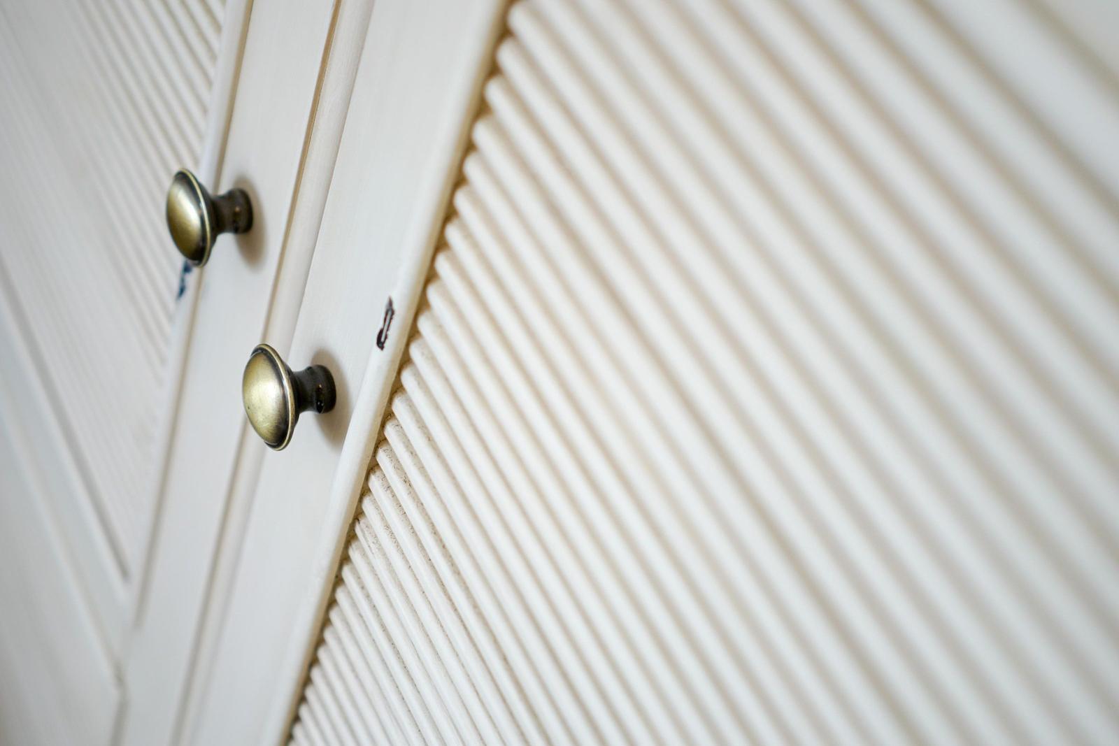 Weißer Schrank mit zwei Messinggriffen und gerippter Front