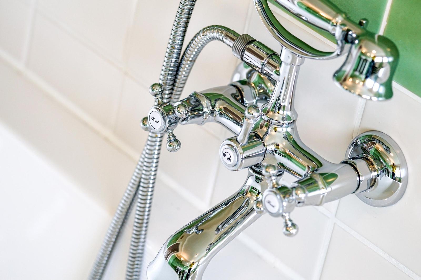 Chromfarbene Duschkopf- und Wasserhähnchenanlage an weißer Wand mit grünem Akzent.