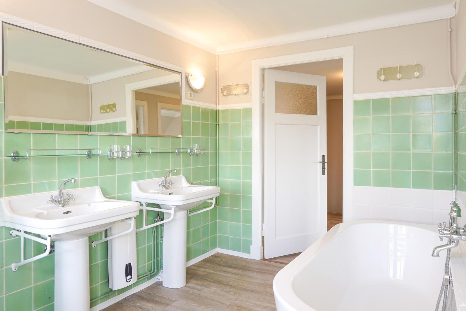 Badezimmer mit zwei Waschbecken, Badewanne und grünen Fliesen.
