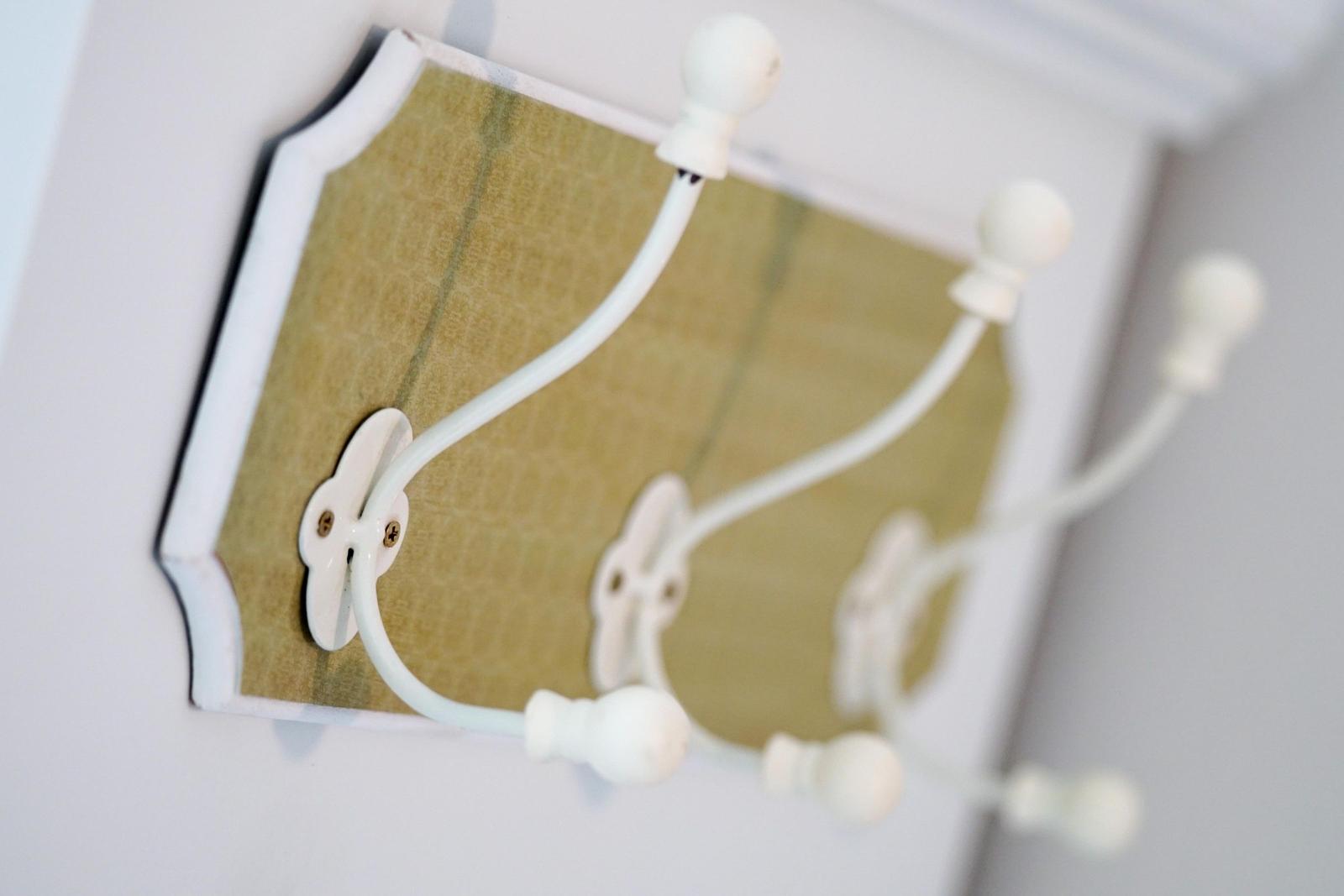 Wandhalter mit drei weißen Haken an einem grünlich-beigen Paneel.