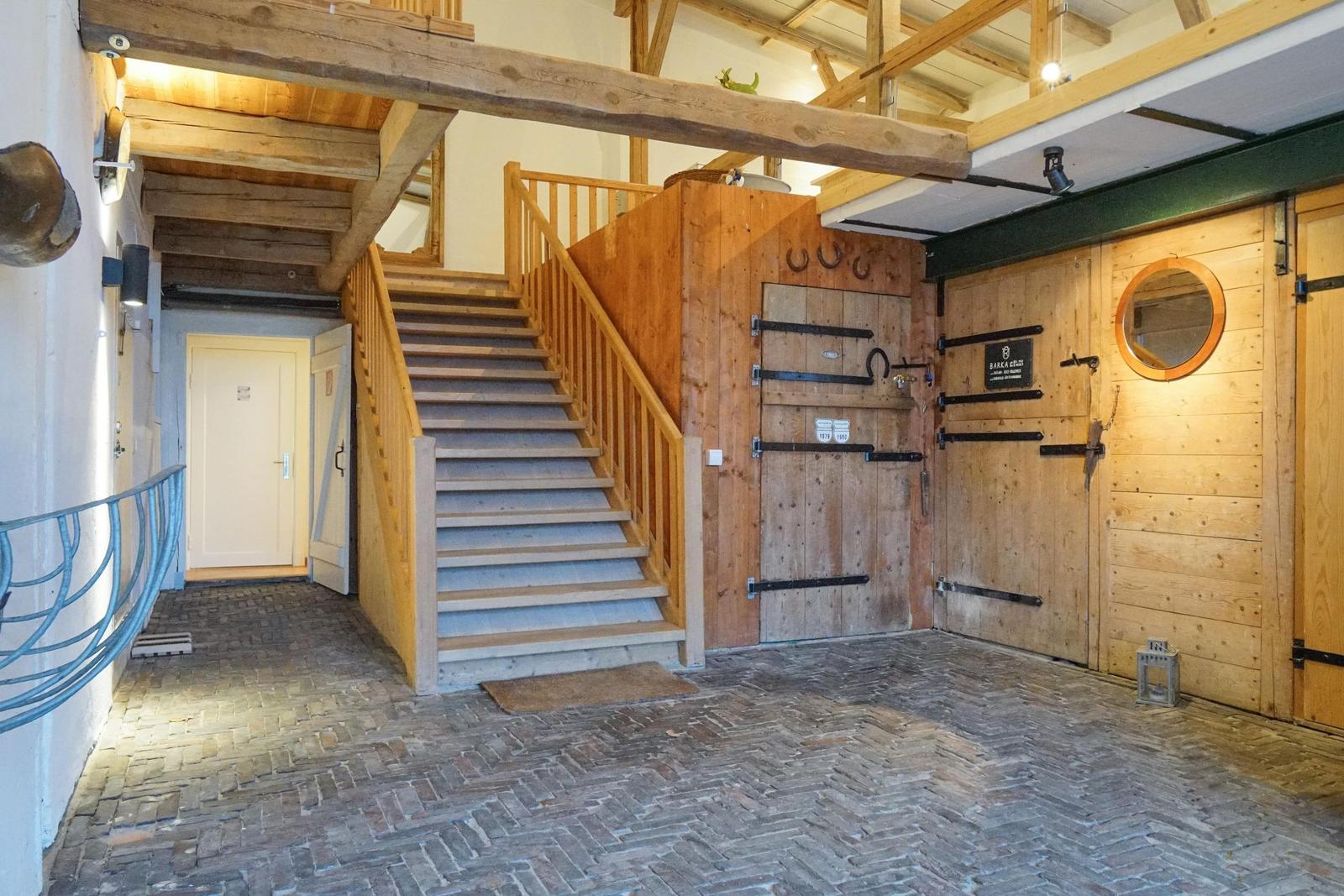 Helle Eingangshalle mit Holztreppe und Pferdestalltüren.