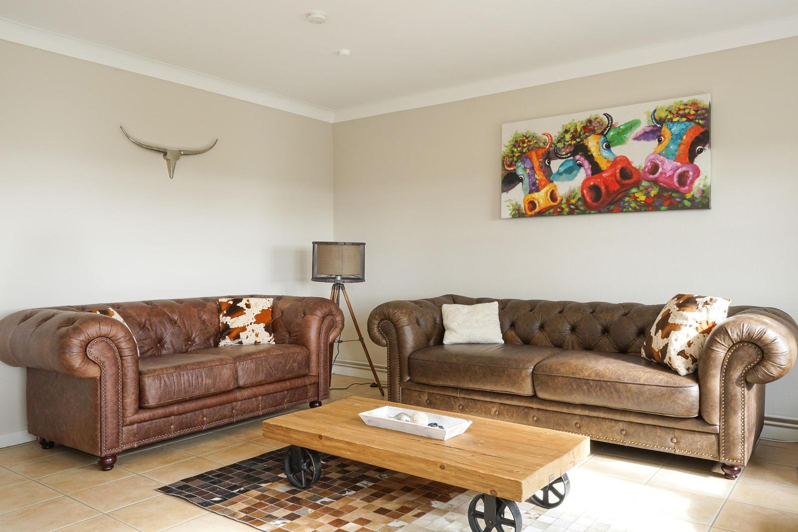 Zwei braune Ledersofas mit Kissen, Holz-Tisch und Wandbild mit Kuhmotiv.