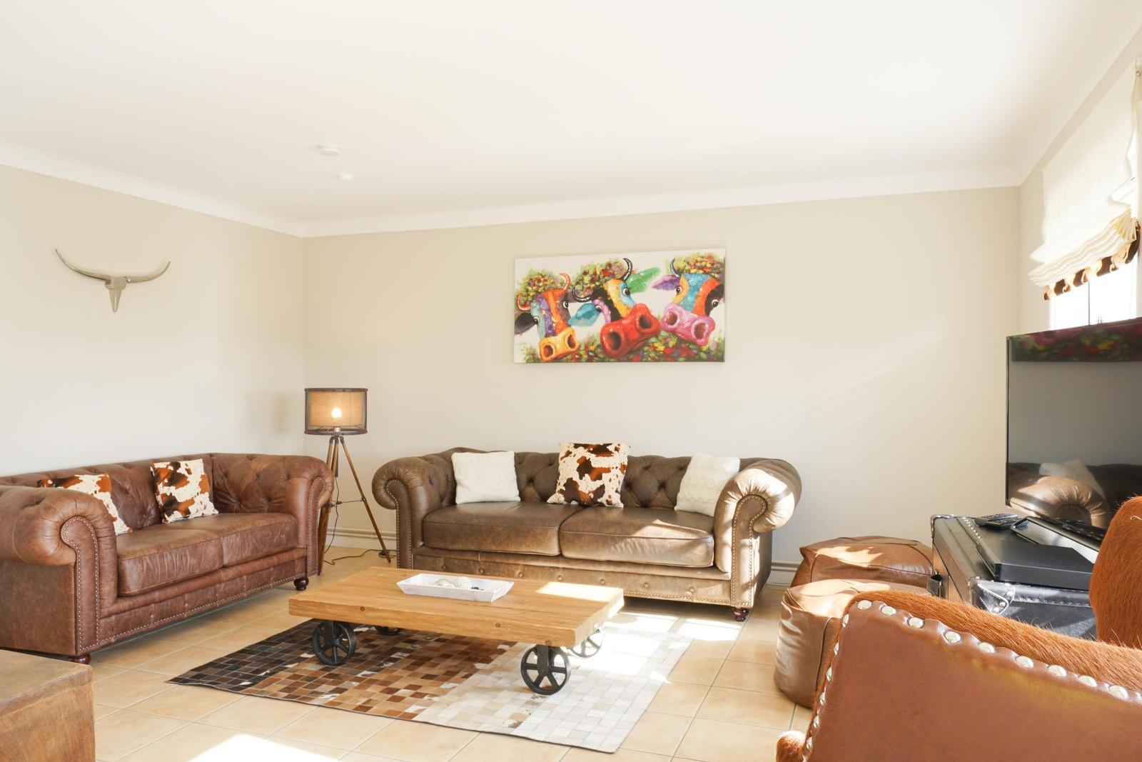 Wohnzimmer mit Ledersofas, Holztisch und Wandbild mit Kuhmotiven.