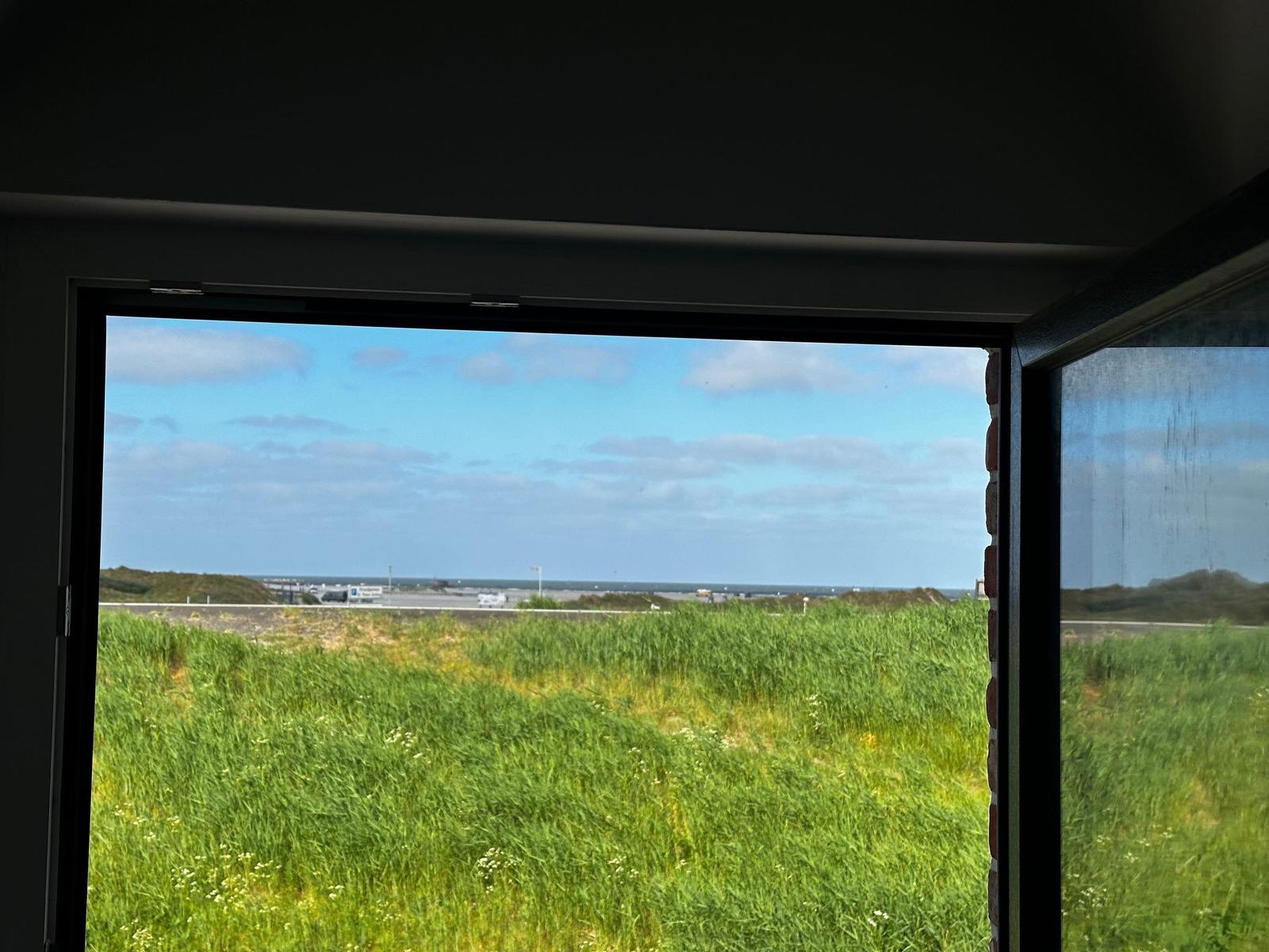 Durch das Fenster blickt man auf ein Grasfeld und einen Flughafen im Hintergrund.