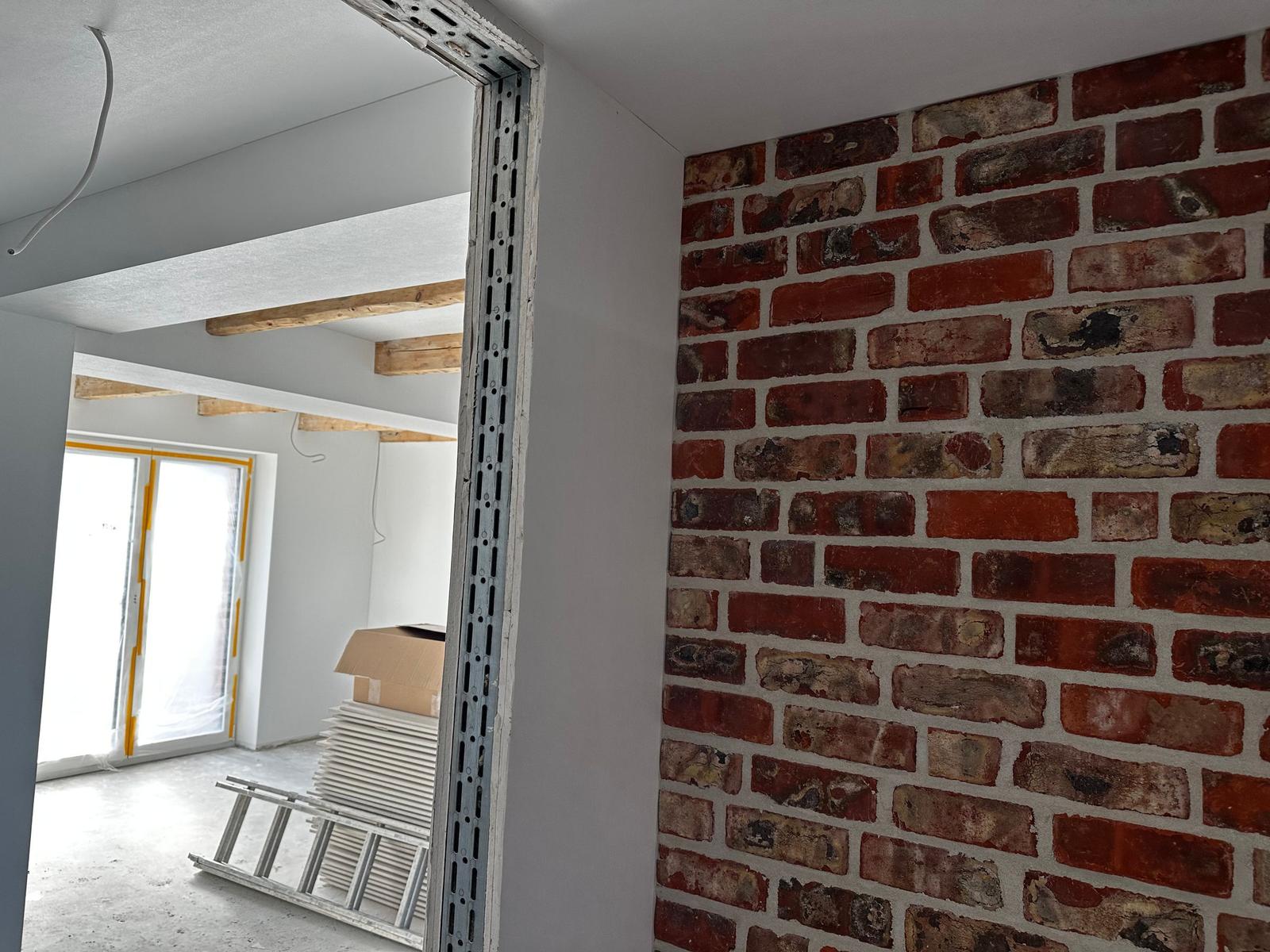 Raum mit sichtbaren Ziegelwand und Baustelle mit Leiter und Karton.