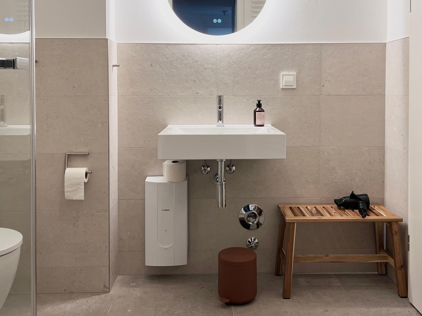 Badezimmer mit Waschbecken, Spiegel, Holzbank und Toilette.