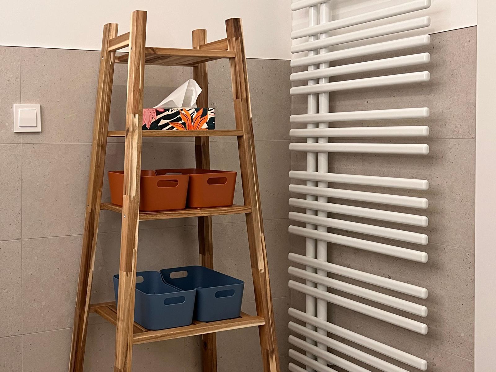 Holzregal mit orangefarbenen und blauen Aufbewahrungskörben neben einem weißen Heizkörper.