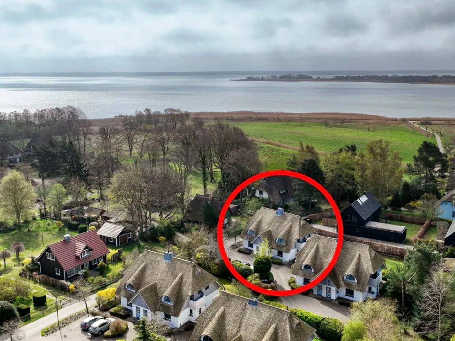 Dorfhaus mit Strohdach und Garten, Blick auf Wasser und Wiesen.