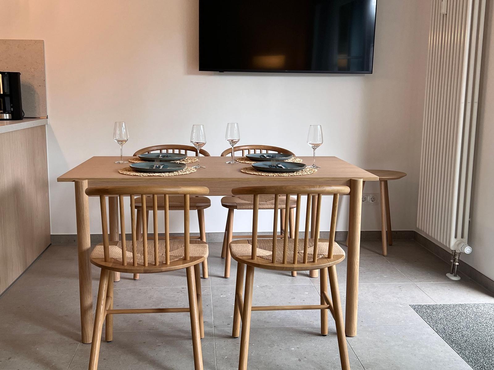 Essbereich mit Holztisch und vier Stühlen, Wandfernseher und Heizkörper