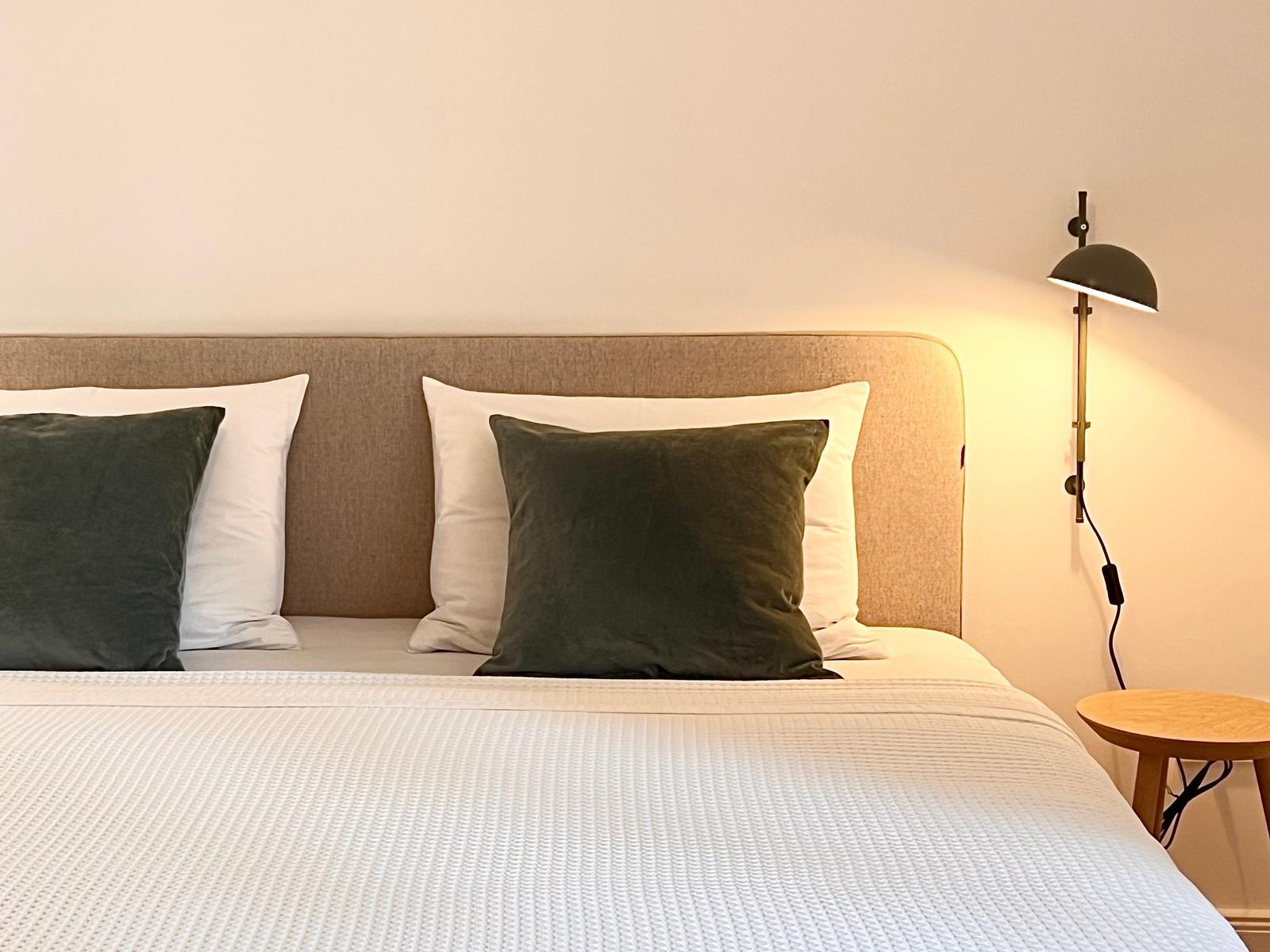 Ein Bett mit weißer Bettwäsche, grünen Kissen und einer Wandlampe.